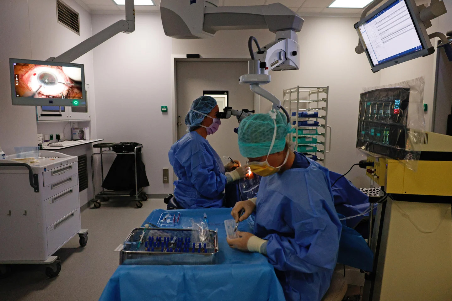 De oogarts opereert door een microscoop. Op een beeldscherm in de operatiekamer kijken de assistenten mee. Meekijken met een staaroperatie